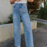 Front view of model wearing the Step Up Wide Leg Jeans which features medium wash denim fabric, a front zipper with button closure, two front pockets, two back pockets, distressed detailing, and wide legs.