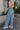 Side view of model wearing the Step Up Wide Leg Jeans which features medium wash denim fabric, a front zipper with button closure, two front pockets, two back pockets, distressed detailing, and wide legs.