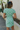 Back view of model wearing the Take Me Higher Top which features green and light blue knit fabric with a checkered pattern, a cropped waist, a round neckline and short sleeves.