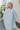 Back view of model wearing the Weekend Wishing Top in Blue which features light blue fabric, monochromatic buttons, a collared neckline, and short sleeves.