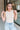 Front view of model wearing the Call It Even Bodysuit in Nude that has stretchy nude fabric, a round neckline, a sleeveless design, and a thong bottom with snap closures.