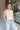 Front view of model wearing the Call It Even Bodysuit in Nude that has stretchy nude fabric, a round neckline, a sleeveless design, and a thong bottom with snap closures.