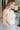 Side view of model wearing the Call It Even Bodysuit in Nude that has stretchy nude fabric, a round neckline, a sleeveless design, and a thong bottom with snap closures.