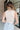 Back view of model wearing the Call It Even Bodysuit in Nude that has stretchy nude fabric, a round neckline, a sleeveless design, and a thong bottom with snap closures.