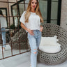 Full body front view of model wearing the Chill Out Top in White that has white burnout fabric, a cropped raw-hem waist, a front pocket, a round neckline, a boxy oversized fit, and short sleeves