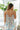Back view of model wearing the Hello Sunshine Top that has purple, blue, orange, green, yellow and ivory fabric with a floral pattern, a peplum hem, a smocked upper, a square neckline and tie straps.