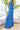 Side view of model wearing the Island Life Pants that have royal blue fabric with a white geometric pattern, a monochromatic side zipper with a hook closure, and wide pant legs