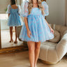 Full front view of model wearing the Wonderland Babydoll Dress that has light blue sheer fabric with a pink rose pattern, light blue lining, a square neck with lace trim, a back zipper and hook closure, and 3/4 puff sleeves with elastic bands