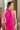 Upper front view of model wearing the Valencia Jumpsuit in Magenta that has magenta fabric, an elastic waist with a tie, pockets a halter neck with a key hole, a back zipper and button closure, and flare pant legs