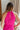 Upper back view of model wearing the Valencia Jumpsuit in Magenta that has magenta fabric, an elastic waist with a tie, pockets a halter neck with a key hole, a back zipper and button closure, and flare pant legs