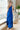 Full body front view of model wearing the Across the Ocean Maxi Dress that has royal blue fabric, maxi length, a ruffle tiered body, a tie around the waist, a smocked upper, one shoulder strap, and royal blue lining.