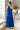 Full body back view of model wearing the Across the Ocean Maxi Dress that has royal blue fabric, maxi length, a ruffle tiered body, a tie around the waist, a smocked upper, one shoulder strap, and royal blue lining.