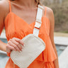 Model is wearing the Carson Sling Bag in Cream that has cream fabric, a gold zipper closure, a striped interior with pockets, a back zippered pocket, and an adjustable strap with gold hardware.