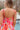 Close up back view of model wearing the Make Bold Moves Jumpsuit features orange, pink, red, purple and turquoise pleated fabric with a marble pattern, a smocked chest with ruffle trim, tie spaghetti straps, and peach lining.