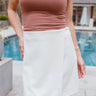 Front view of model wearing the You're Go To White Skirt which features off white fabric, off white lining, a front overlay, and a monochromatic side zipper with a hook closure.