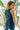 Close up back view of model wearing the Ready To Go Denim Jumpsuit in Indigo which features indigo denim fabric, waistband, high round neckline, sleeveless, back zipper closure and flare pant leg.