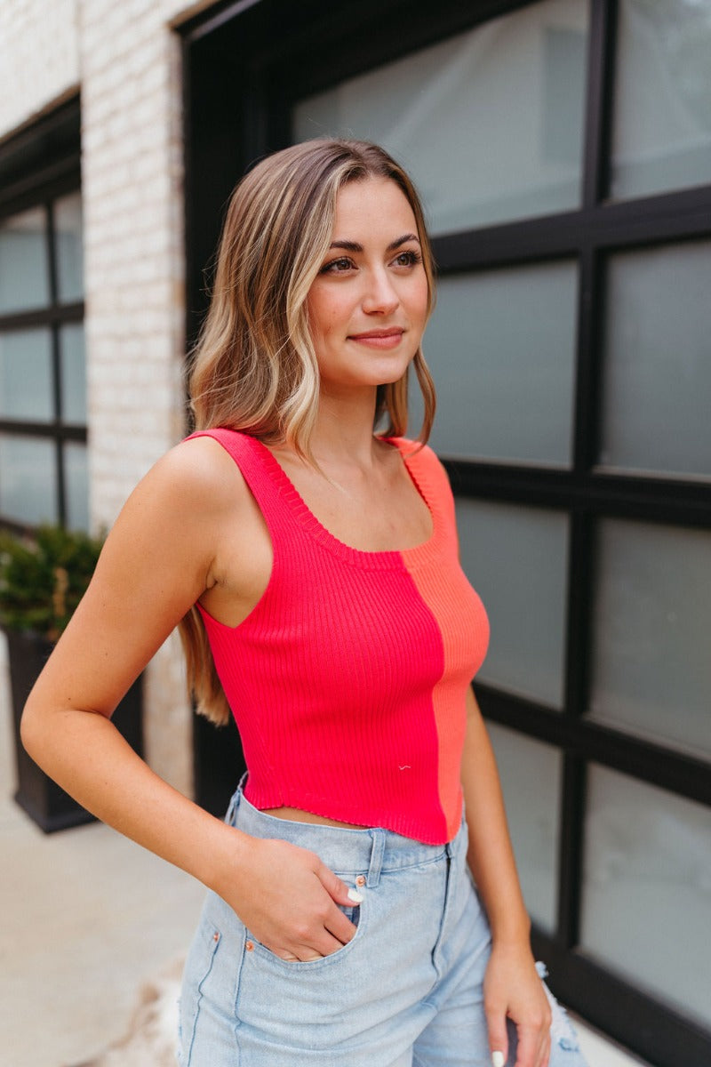 Side view of model wearing the Chasing Sunshine Tank which features ribbed fabric with orange and pink color blocking, a cropped waist, a round neckline, and thick straps.