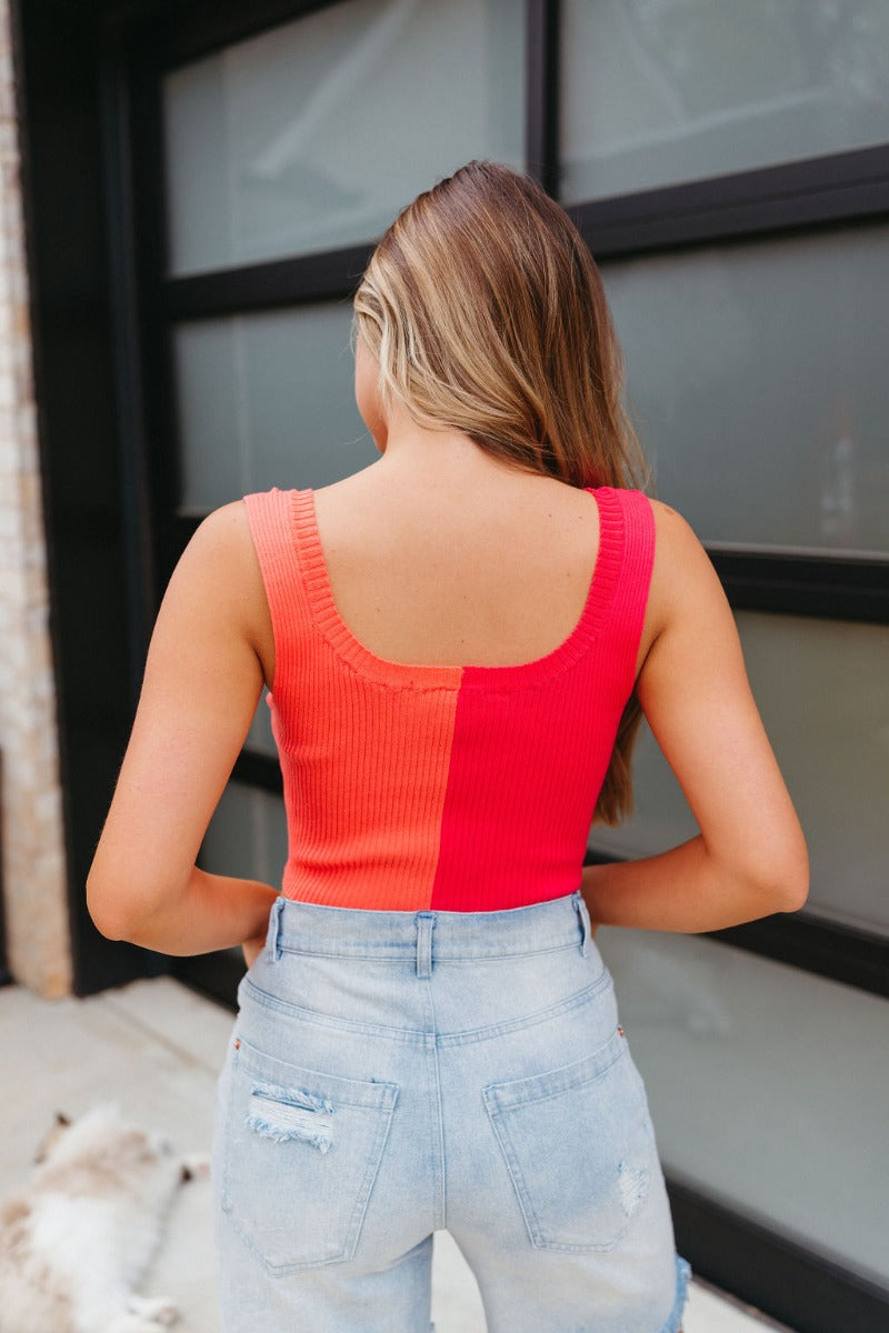 Back view of model wearing the Chasing Sunshine Tank which features ribbed fabric with orange and pink color blocking, a cropped waist, a round neckline, and thick straps.