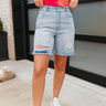 Front view of model wearing the Day to Day Shorts which features light denim wash fabric, a front zipper and button closure, two front pockets, two back pockets, distressed details, midi length and a distressed hem.