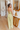 Full body back view of model wearing the Step On It Jumpsuit which features olive green fabric, two front pockets, two back pockets, an elastic waistband, a square neckline, spaghetti straps, an open back with ties, and flared pant legs.