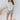 Full body front view of model wearing the All For You Top that has white cotton fabric, a scooped hem, a smocked upper chest, a round neckline and short flare sleeves