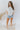Full body front view of model wearing the All For You Top that has white cotton fabric, a scooped hem, a smocked upper chest, a round neckline and short flare sleeves
