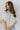 Front view of model wearing the All For You Top that has white cotton fabric, a scooped hem, a smocked upper chest, a round neckline and short flare sleeves