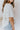 Side view of model wearing the All For You Top that has white cotton fabric, a scooped hem, a smocked upper chest, a round neckline and short flare sleeves