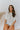 Front view of model wearing the All For You Top that has white cotton fabric, a scooped hem, a smocked upper chest, a round neckline and short flare sleeves