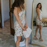 Full body side view of model wearing the Endless Love Dress that has beige, peach and green jacquard fabric with a floral pattern, a front slit, one shoulder with a spaghetti strap, and a back zipper