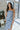 Front view of model wearing the Better This Way Dress which features light blue, dark blue and cream brocade fabric with a floral design, a midi-length hem, a front slit, a straight strapless neckline, and a monochromatic back zipper.