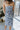 Back view of model wearing the Better This Way Dress which features light blue, dark blue and cream brocade fabric with a floral design, a midi-length hem, a front slit, a straight strapless neckline, and a monochromatic back zipper.