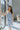 Full body view of model wearing the Better This Way Dress which features light blue, dark blue and cream brocade fabric with a floral design, a midi-length hem, a front slit, a straight strapless neckline, and a monochromatic back zipper.