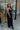 Full body view of model wearing the Sweet Escape Jumpsuit which features black plisse fabric, side pockets, a v neckline, adjustable spaghetti straps, and wide pant legs.