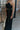Side view of model wearing the Sweet Escape Jumpsuit which features black plisse fabric, side pockets, a v neckline, adjustable spaghetti straps, and wide pant legs.