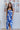 Full body view of model wearing the Meet Me At The Beach Skirt which features white fabric with a blue leaf design, white lining, midi length, a slit on the side, and a wrap waist with a tie and button closure.