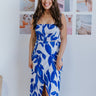 Full body view of model wearing the Meet Me At The Beach Skirt which features white fabric with a blue leaf design, white lining, midi length, a slit on the side, and a wrap waist with a tie and button closure.