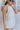 Side view of model wearing the On Island Time Romper which features ivory fabric, textured front pockets, a halter neckline that ties around the neck, and an open back with an elastic band.