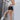 Full body side view of model wearing the Rolling Stones Shorts which features black denim fabric, silver stud details on the side, a front zipper and button closure, belt loops, two front pockets, two back pockets and a frayed hem.