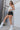 Full body side view of model wearing the Rolling Stones Shorts which features black denim fabric, silver stud details on the side, a front zipper and button closure, belt loops, two front pockets, two back pockets and a frayed hem.