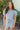 Front view of model wearing the She's A Star Denim Romper that has light denim fabric, pockets on each side, silver buttons, silver sequin star patches, a collared neckline, short puff sleeves, and denim tie belt around the waist