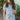 Front view of model wearing the She's A Star Denim Romper that has light denim fabric, pockets on each side, silver buttons, silver sequin star patches, a collared neckline, short puff sleeves, and denim tie belt around the waist