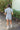 Full back view of model wearing the She's A Star Denim Romper that has light denim fabric, pockets on each side, silver buttons, silver sequin star patches, a collared neckline, short puff sleeves, and denim tie belt around the waist