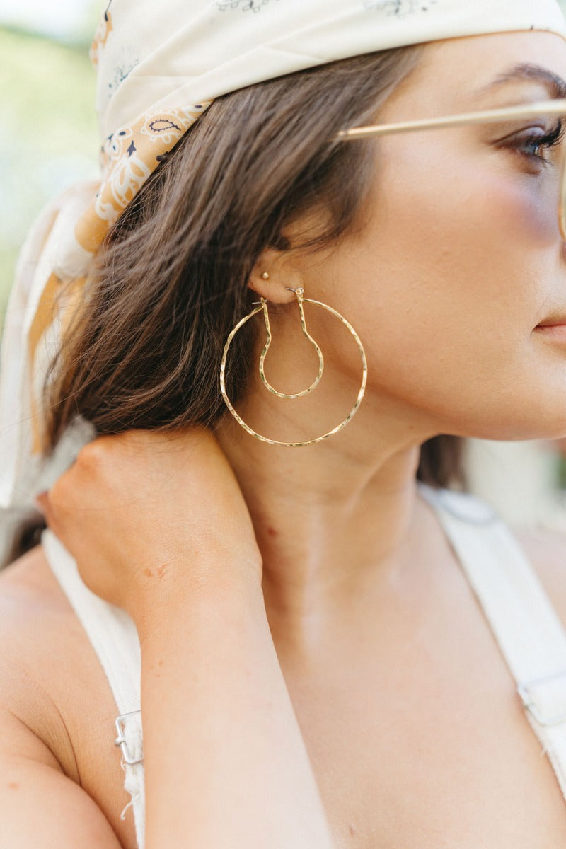 Side view of model wearing the Hepburn Hoop Earring which features large closed hoop with gold hammered design.