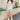 Full body front view of model wearing the Nashville Graphic Tee that has cream fabric, a round, and short sleeves. Graphic says Music City and Nashville, TN with pink roses, light blue leaves and a guitar outlined in brown