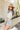 Side view of model wearing the Nashville Graphic Tee that has cream fabric, a round, and short sleeves. Graphic says Music City and Nashville, TN with pink roses, light blue leaves and a guitar outlined in brown