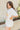Side view of model wearing the Nashville Graphic Tee that has cream fabric, a round, and short sleeves. Graphic says Music City and Nashville, TN with pink roses, light blue leaves and a guitar outlined in brown