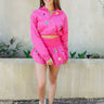 Full body front view of model wearing the Star-Struck Pullover that has fuchsia nylon fabric, multi-colored sequin star patches, a cropped waist with a drawstring tie, a high neck with a half zip up, and long sleeves with cuffs.