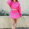 Full body front view of model wearing the Star-Struck Skort that has fuchsia nylon fabric, multi-colored sequin star patches, fuchsia shorts lining, and a high-rise smocked waistband
