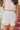 Front view of model wearing the Once In A Lifetime Pleated Shorts that feature white pleated fabric, white shorts lining, and a monochromatic back zipper with a hook closure